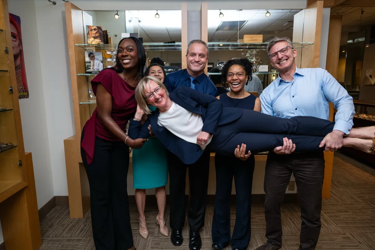 The Voorthuis opticians laughing as they lift the shop's owner off the ground in the showroom