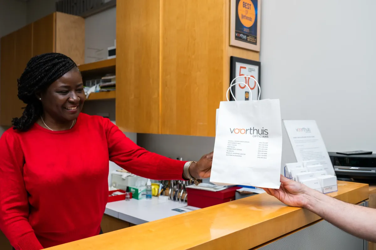 A Voorthuis optician handing a branded bag to a smiling customer at the counter